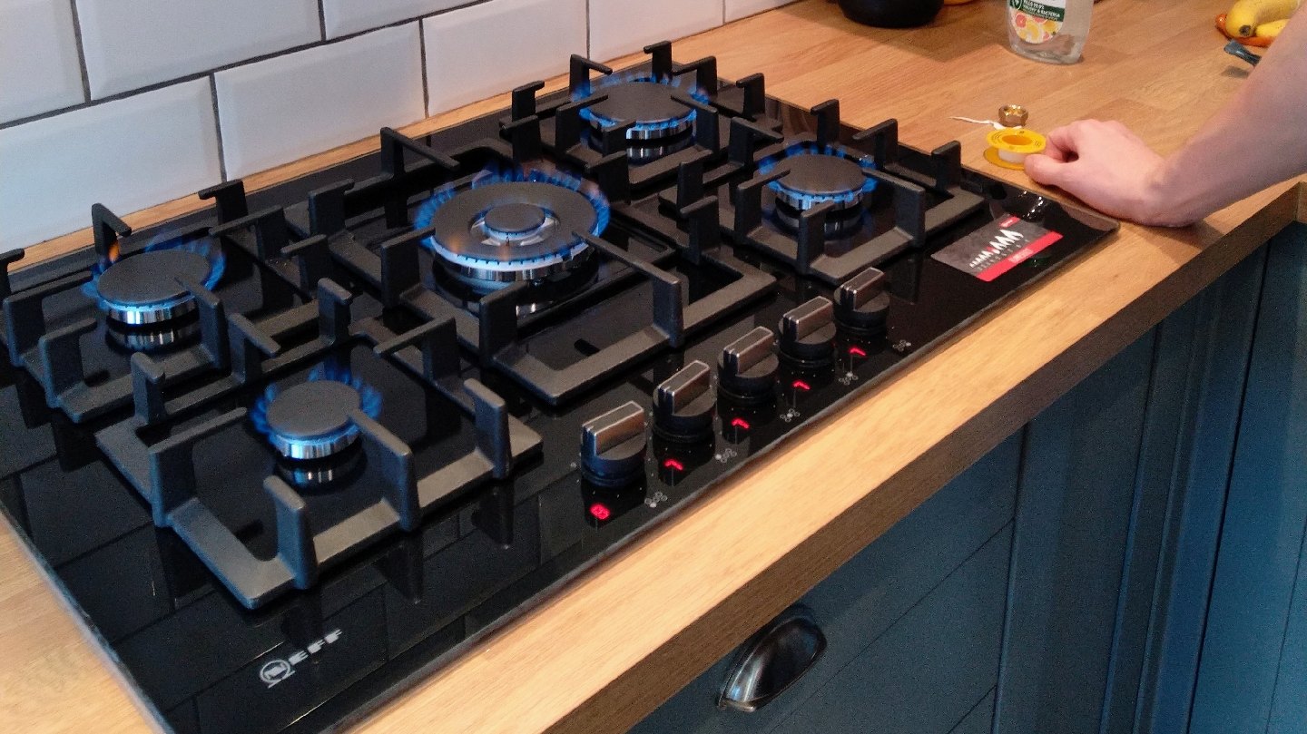 A five-burner gas hob fitted in an oak worktop, with every ring alight